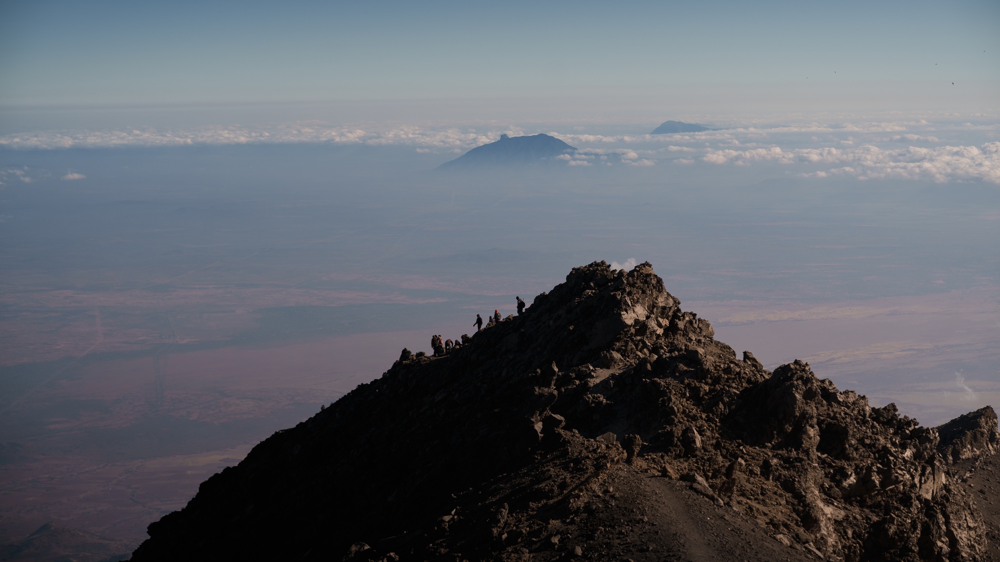 Hikers climbing mount meru in tanzania, africa, with kilimanjaro in background